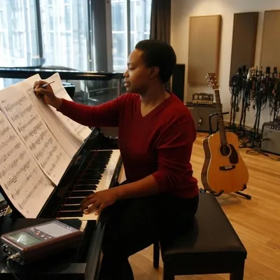Compositora escribiendo sobre una partitura en un piano de cola dentro de un estudio tranquilo